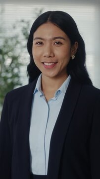Portrait of positive Asian businesswoman smiles surely in corporate environment vertical shot. Japanese woman department manager stands in company office