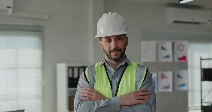 Portrait of Middle Eastern bearded construction manager in hard hat and safety vest in office. Specialist crosses arms and looks at camera with confidence