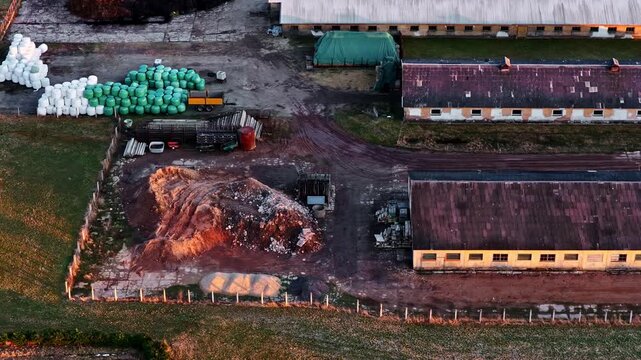 Rural farm with barns, silage bales, and a large manure heap in aerial view on golden hour