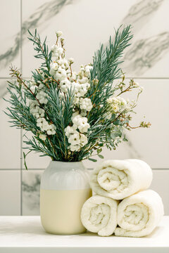 A collection of elegant matte gray ceramic cosmetic bottles and jars with bamboo lids is artfully arranged with delicate white dried flowers against a clean, neutral background