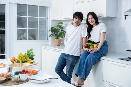 Happy portrait of loving young asian of having fun standing a cheerful preparing food and enjoy cook cooking with vegetables, meat, bread while standing on a kitchen Condo life or home