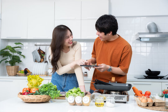 Happy portrait of loving young asian of having fun standing a cheerful preparing food and enjoy cook cooking with vegetables, meat, bread while standing on a kitchen Condo life or home