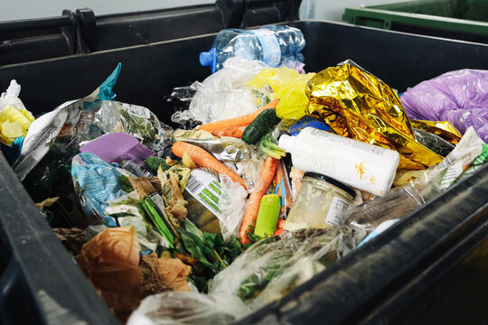 Overflowing garbage container with food and plastic waste. Household trash and recycling problem. Environmental pollution concept. Mixed rubbish inside dumpster close up. Waste management issue