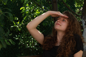 Naklejka premium Young woman looks up while sitting in a lush garden during a sunny afternoon enjoying nature and the outdoors