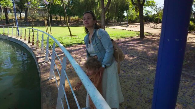 A Loving Mother and Her Curious Child Explore a Serene Park Pond.