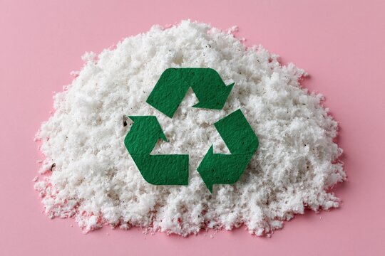 Green recycle symbol placed on shredded white pulp on pink background for environmental poster, sustainability campaign and eco design mockup
