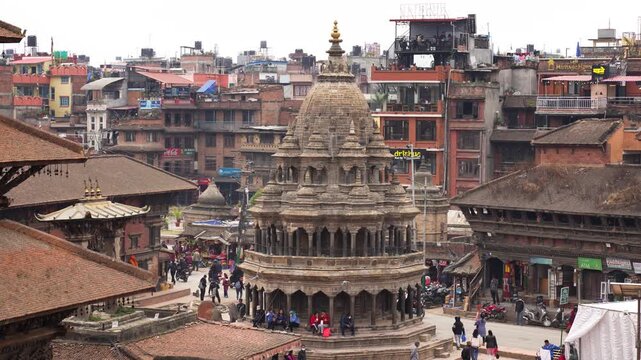 Kathmandu, Nepal - 19 May 2026: View of a historic stone temple with people sitting on its base, surrounded by traditional brick buildings and rooftops in the city center.
