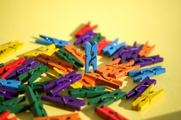 Fototapeta premium Colorful Wooden Clothespins on Yellow Background with One Blue Pin Standing Upright 