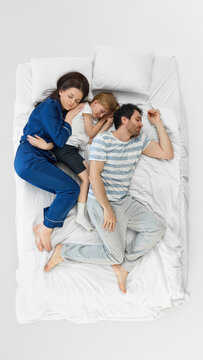 Family sleep arrangement on white bed with mother child and father resting apart. Concept of parenting routine, co-sleeping, bedroom space, sleep quality, and family wellness.