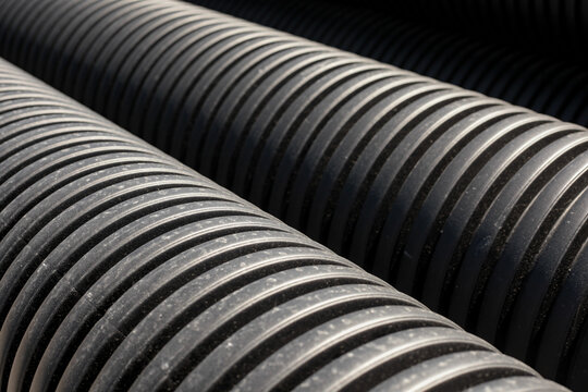 Rows of black corrugated plastic drainage pipes stacked together. Industrial background with geometric texture of construction materials for infrastructure projects.