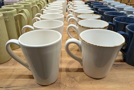 Grupo de tazas de caf&eacute; de cer&aacute;mica de varios colores expuestas en una mesa de madera 