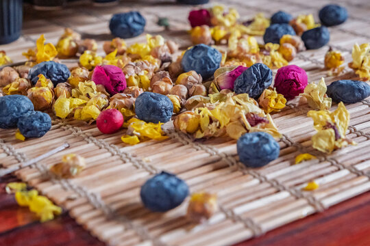 Flowers and berries scattered on a bamboo mat with a black vase on a wooden table