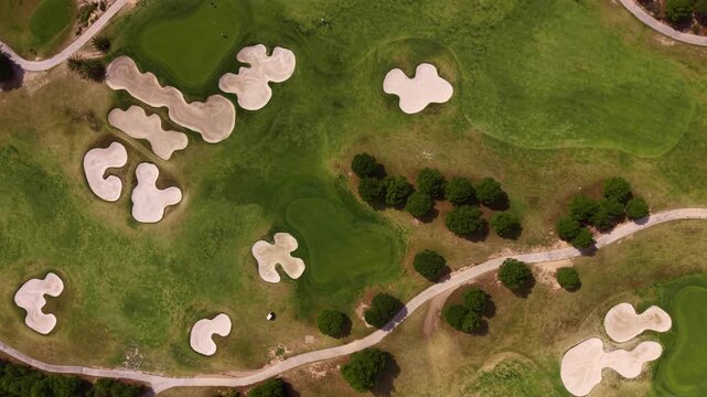 Overhead top-down view of a golf course featuring multiple sand bunkers, lush green fairways, scattered trees, and winding cart paths across the landscape