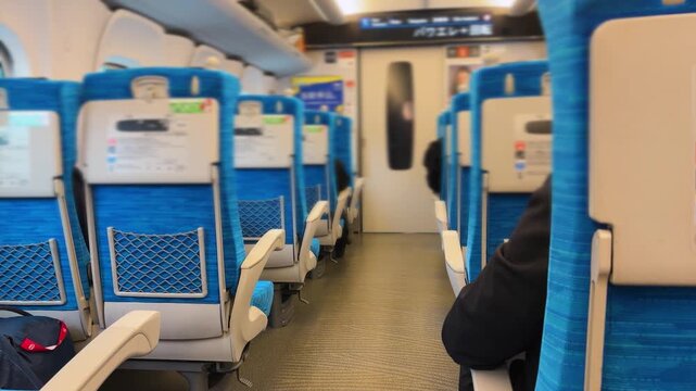 Interior of a Japanese Shinkansen bullet train heading from Fukuoka to Osaka. Blue comfortable passenger seats in a row in a clean modern carriage. Electric information display showing travel details.