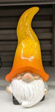 Vista de cerca de un decorativo gnomo de jard&iacute;n de cer&aacute;mica, con un enorme sombrero amarillo que, junto con la barba blanca, le tapa el rostro, en el estante de una tienda 