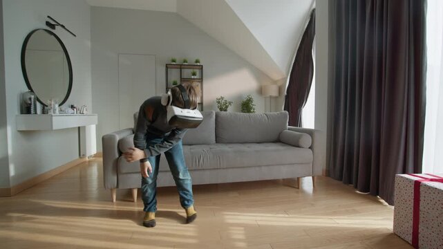 Person wearing virtual reality headset moves arms and legs in a modern living room with a sofa and gift box. The lively scene conveys futuristic engagement, digital immersion and the playful energy