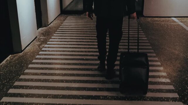 Anonymous man walking with a suitcase along a striped pathway in a dimly lit underground area