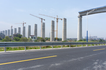 Fototapeta premium Construction site of concrete bridge piers with cranes beside a highway road