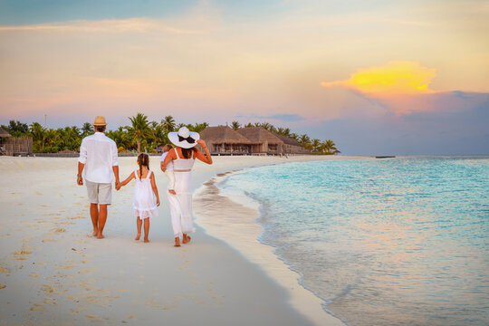 A beautiful family walks on a tropical paradise beach in the Maldives islands during sunset time as a travel concept