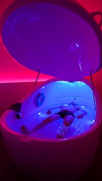 Vertical: caucasian man floating and relaxing in hyper-saline floatation therapy pod, indoor, static shot, medium shot