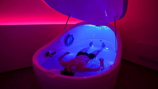 Man floating in sensory deprivation tank with colored lighting during relaxation therapy session