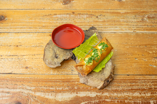 A woven bamboo tray displays a row of Vietnamese spring rolls, with a small container of fish sauce and wooden chopsticks resting on the edge of the plate.