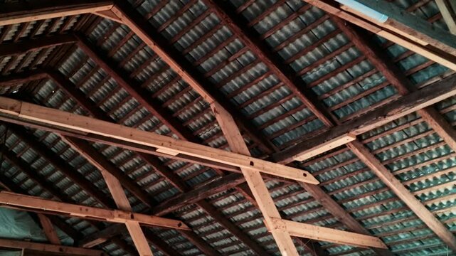 Dark and dusty interior of an old barn with wooden roof structure and corrugated metal ceiling
