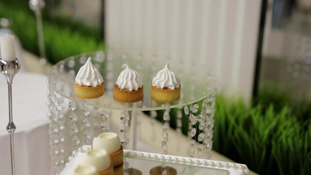 Waiter in gloves placing elegant meringue tartlets on a crystal glass stand