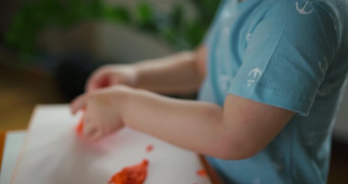 Funny little boy with painted mustache playing with orange modeling clay