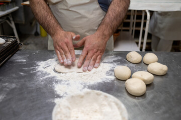 Fototapeta premium Baker hands kneading bread dough on a floured metal surface with balls of dough ready, preparing bakery products