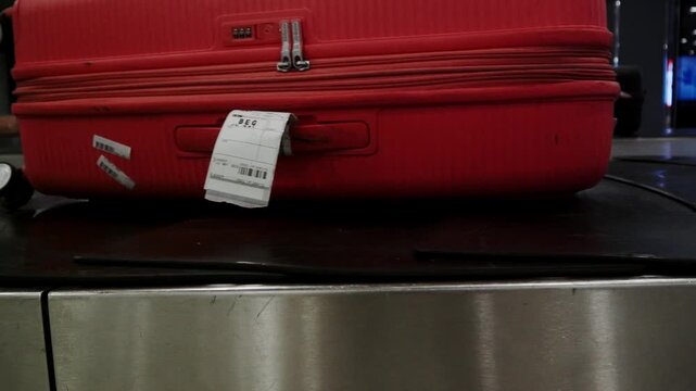 Red suitcase with a luggage tag moving along the baggage carousel in Tbilisi airport terminal.