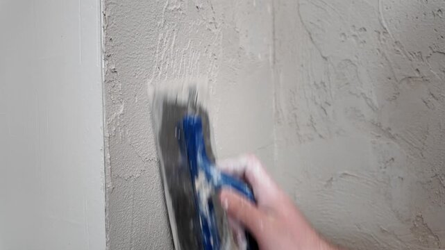 A person is applying texture to a wall with a trowel in a home project during the evening. This process shows the steps taken in wall finishing.