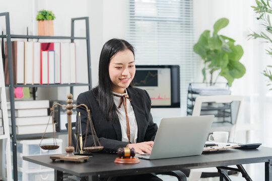 Lawyer Working at Desk: A professional female lawyer diligently works on her laptop at a well-organized desk, surrounded by legal books, a scale of justice, and a gavel.