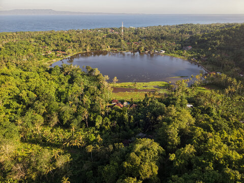 Aerial view of Danau Yeh Malet lake in Karangasem Bali surrounded by lush tropical forest and coconut trees near the ocean coast