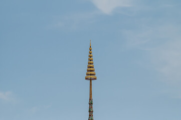 Obraz premium Golden multi-tiered umbrella spire on top of Thai temple roof against blue sky background.