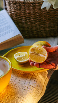 Hand holding a juicy lemon half over a yellow plate with citrus fruit and drink