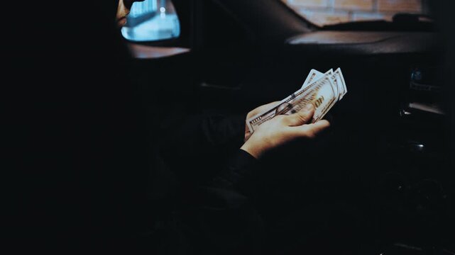 Criminal inside a dark car counting stolen money as police car lights flash, signaling his arrest