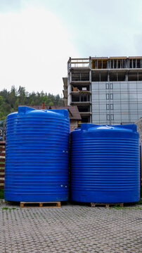 Two large blue plastic water tanks stand on pallets in front of a construction site