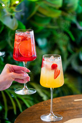 Two vibrant spritz cocktails in wine glasses filled with ice, garnished with citrus and strawberry...