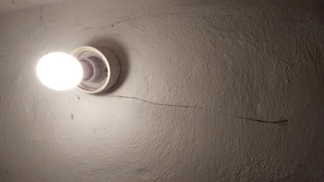 Glowing light bulb on a textured ceiling with a long spider web hanging across the frame