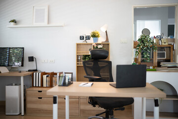 Fototapeta premium A bright, organized home office featuring wooden desks, ergonomic chair, laptop, monitor, and indoor plants, ideal for remote work and productivity concepts