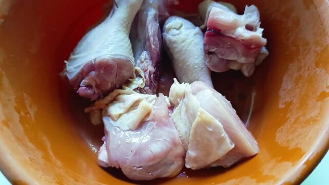 Raw chicken pieces inside an orange plastic bowl prepared for cooking