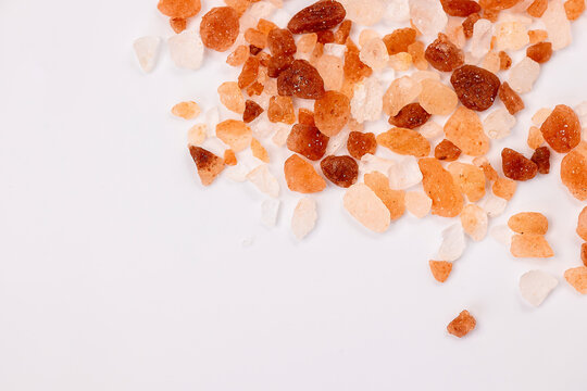 Pink Himalayan salt crystals scattered on white background with large copy space. Natural mineral seasoning texture for gourmet cooking and wellness concepts.
