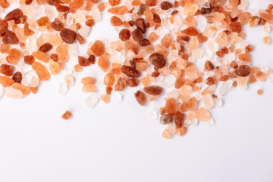 Pink Himalayan salt crystals scattered on white background with copy space. Natural mineral seasoning texture for gourmet cooking, wellness and healthy lifestyle concepts.