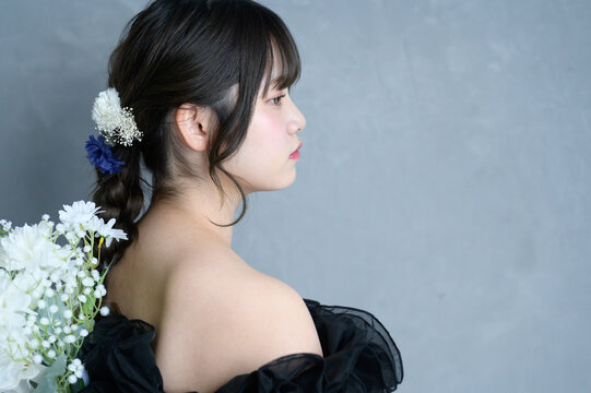 グレー背景でブーケを持つ黒いドレスを着た日本人女性