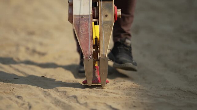 Dhangadhi, Nepal - 19 May 2026: View of a manual seed planter tool being used in sandy soil with a worker walking behind it.