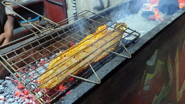 Fresh seasoned fish fillet grilling over hot glowing charcoal embers in a cinematic slow motion video clip capturing the smoky cooking process of traditional street food