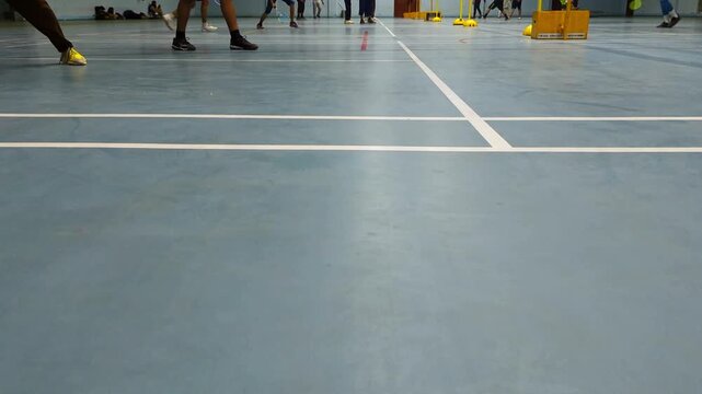 Active badminton players moving swiftly across the blue court surface during a competitive match while wearing athletic sneakers in this high quality four k video clip