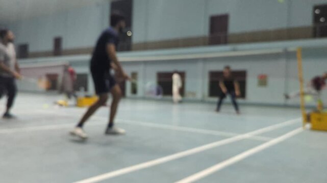 Badminton players in  blur motion during an intense match inside a large indoor sports facility capturing athletic performance and competitive spirit during a fast paced game session
