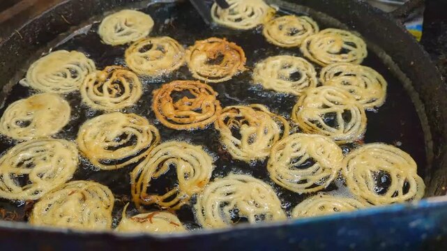 Crispy jalebi spirals frying in a large pan of hot bubbling oil captured in a cinematic 4k video sequence showing the traditional Indian sweet preparation process